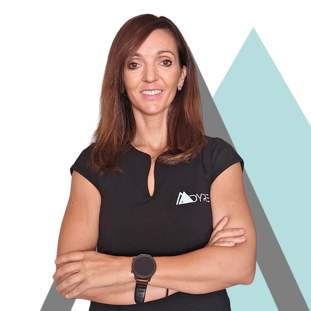 Una mujer con cabello largo y castaño, que viste un top negro con un logotipo, se encuentra de pie con confianza con los brazos cruzados sobre un fondo blanco con formas geométricas.