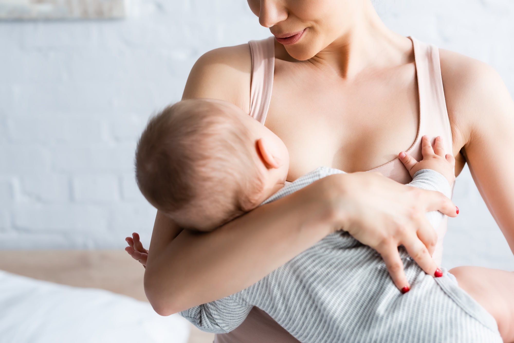 fisioterapia pediatrica Una madre amamanta a su bebé en brazos. El bebé lleva un mono de rayas. El fondo está suavemente difuminado y la escena transmite una sensación de calidez y ternura. Lactancia. Daganzo Adyre